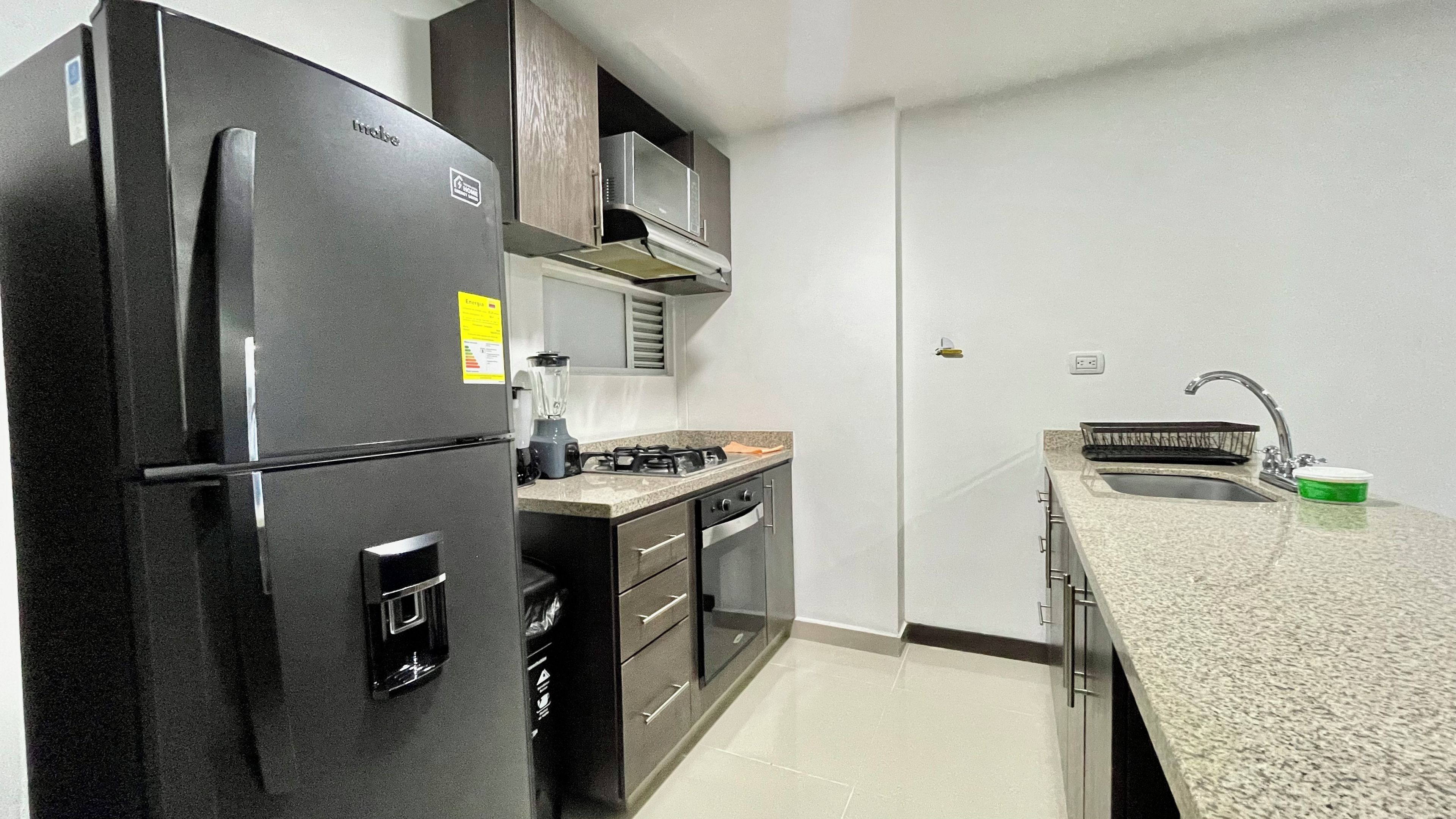 Una cocina compacta equipada con refrigerador, estufa, horno microondas y pileta.