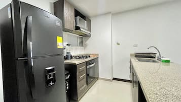 Una cocina compacta equipada con refrigerador, estufa, horno microondas y pileta.