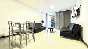 A modern living room with a dining table, chairs, a sofa, and a TV mounted on the wall. - Conquistadores Apartamentos (Medellín)