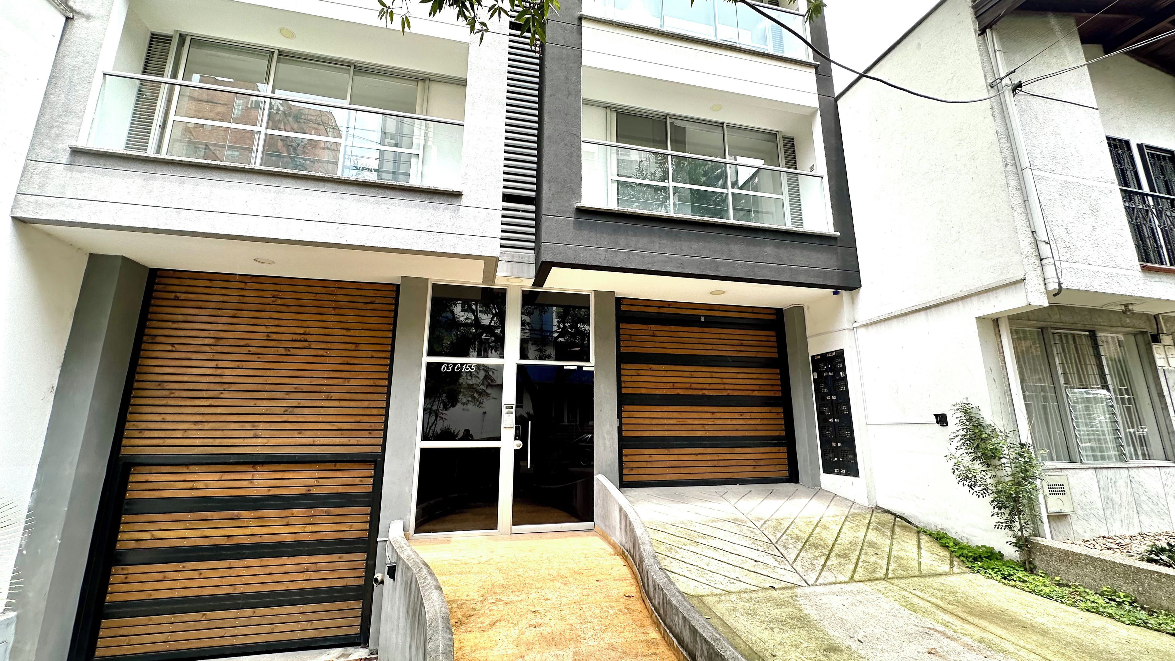 Um edifício moderno com duas grandes portas de garagem, uma pequena entrada e uma escada de concreto que leva à entrada.