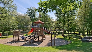 A playground with a slide and climbing structures surrounded by grass and trees.