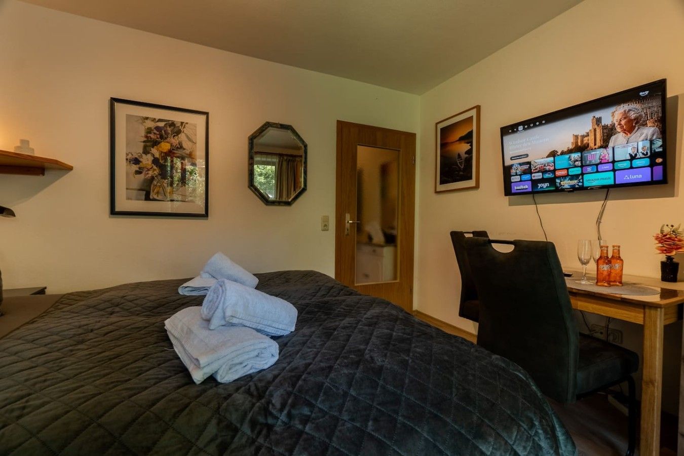 A hotel room with a bed, a desk, a chair, a television, and framed artwork on the walls.