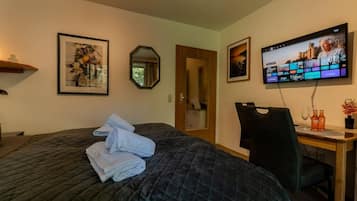 A hotel room with a bed, a desk, a chair, a television, and framed artwork on the walls.