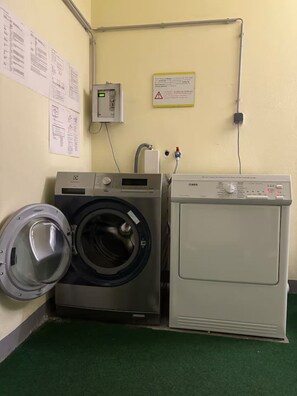 A laundry room with a front-loading washing machine and a top-loading dryer, connected to a wall-mounted electrical panel.