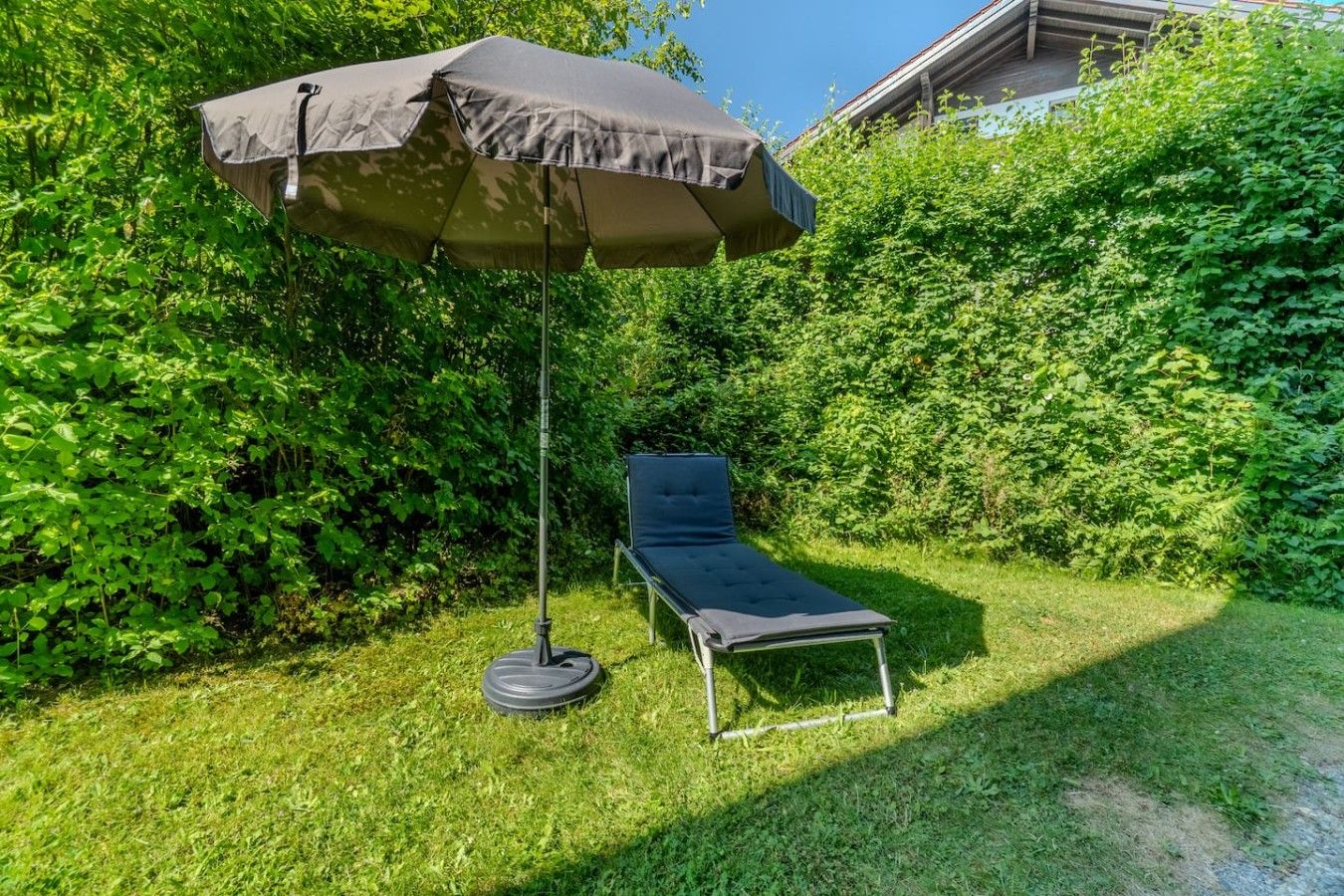 Un jardin avec une chaise longue et un grand parasol.