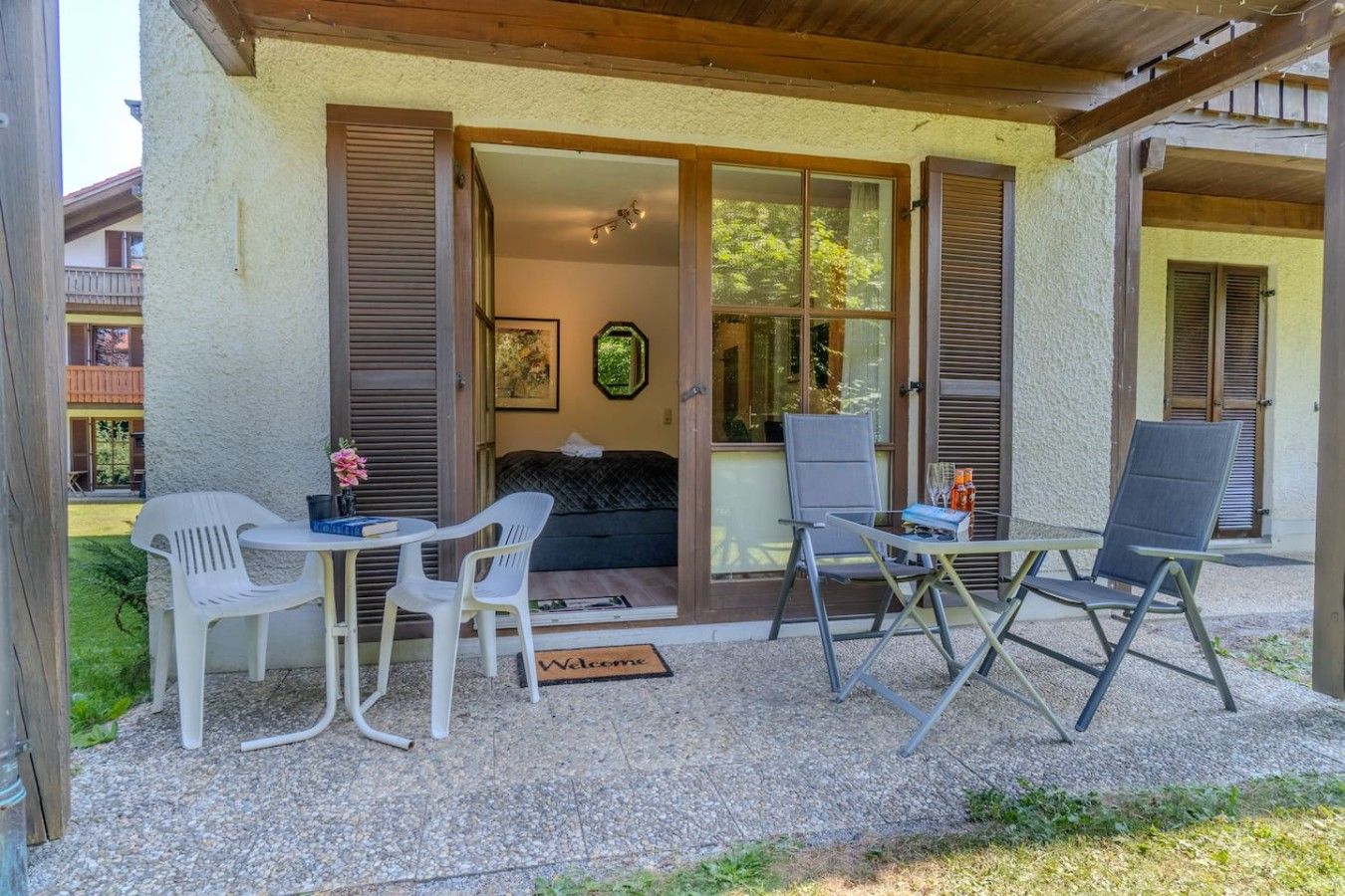 A covered outdoor seating area with a table and chairs, a sofa, and a door leading to a room.