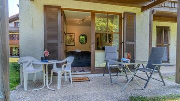 A covered outdoor seating area with a table and chairs, a sofa, and a door leading to a room.