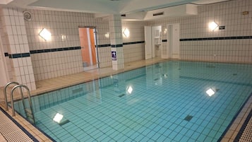 Une piscine intérieure avec des murs et un sol carrelés, et une porte visible donnant sur une autre pièce.