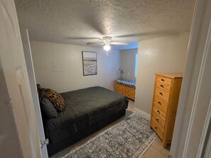 A bedroom with a bed, a dresser, a ceiling fan, and a rug. - The Hidden Gem: Cozy Blue Cottage Sleeps 6, 10 min. to OU . Pet friendly (Noble)