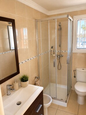 A modern bathroom with a glass-enclosed shower, a toilet, a sink with a mirror, and a potted plant. - Oliva Nova MET & Beach - Apartment for 4 people, 400 m from the beach and 50 MET from the Costa Blanca (VC)