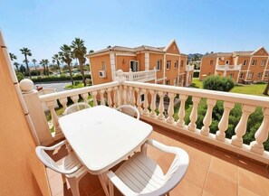 A balcony with a white table and chairs, overlooking a residential area with houses and palm trees. - Oliva Nova MET & Beach - Apartment for 4 people, 400 m from the beach and 50 MET from the Costa Blanca (VC)