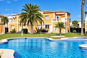 A swimming pool with a curved edge, surrounded by a well-maintained lawn and palm trees. - Oliva Nova MET & Beach - Apartment for 4 people, 400 m from the beach and 50 MET from the Costa Blanca (VC)