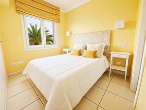 A hotel room with a bed, bedside tables, a window with curtains, and a view of palm trees. - Oliva Nova MET & Beach - Apartment for 4 people, 400 m from the beach and 50 MET from the Costa Blanca (VC)