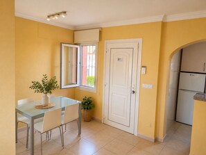 A compact kitchen with a refrigerator, a dining table with chairs, a potted plant, and a door with a window. - Oliva Nova MET & Beach - Apartment for 4 people, 400 m from the beach and 50 MET from the Costa Blanca (VC)