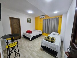 Quarto compacto com duas camas, uma mesinha e uma cadeira.