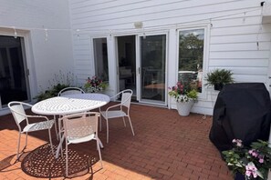 Eine Terrasse mit einem runden Tisch und Stühlen, einem Grill und Kübelpflanzen.