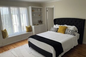 Ein Schlafzimmer mit einem Bett, einem Fenster mit Vorhängen, einem weißen Schrank und einer Tür.