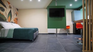A bedroom with a bed, a green wall-mounted TV, and a red chair.