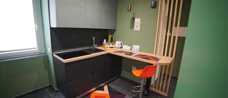 Cocina pequeña con encimera negra, lavabo y taburete.