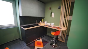 Une cuisine de taille réduite avec un plan de travail noir, un évier et un tabouret de bar.