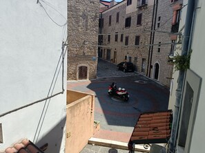 Une rue étroite avec un rond-point, des bâtiments en pierre et un scooter garé.
