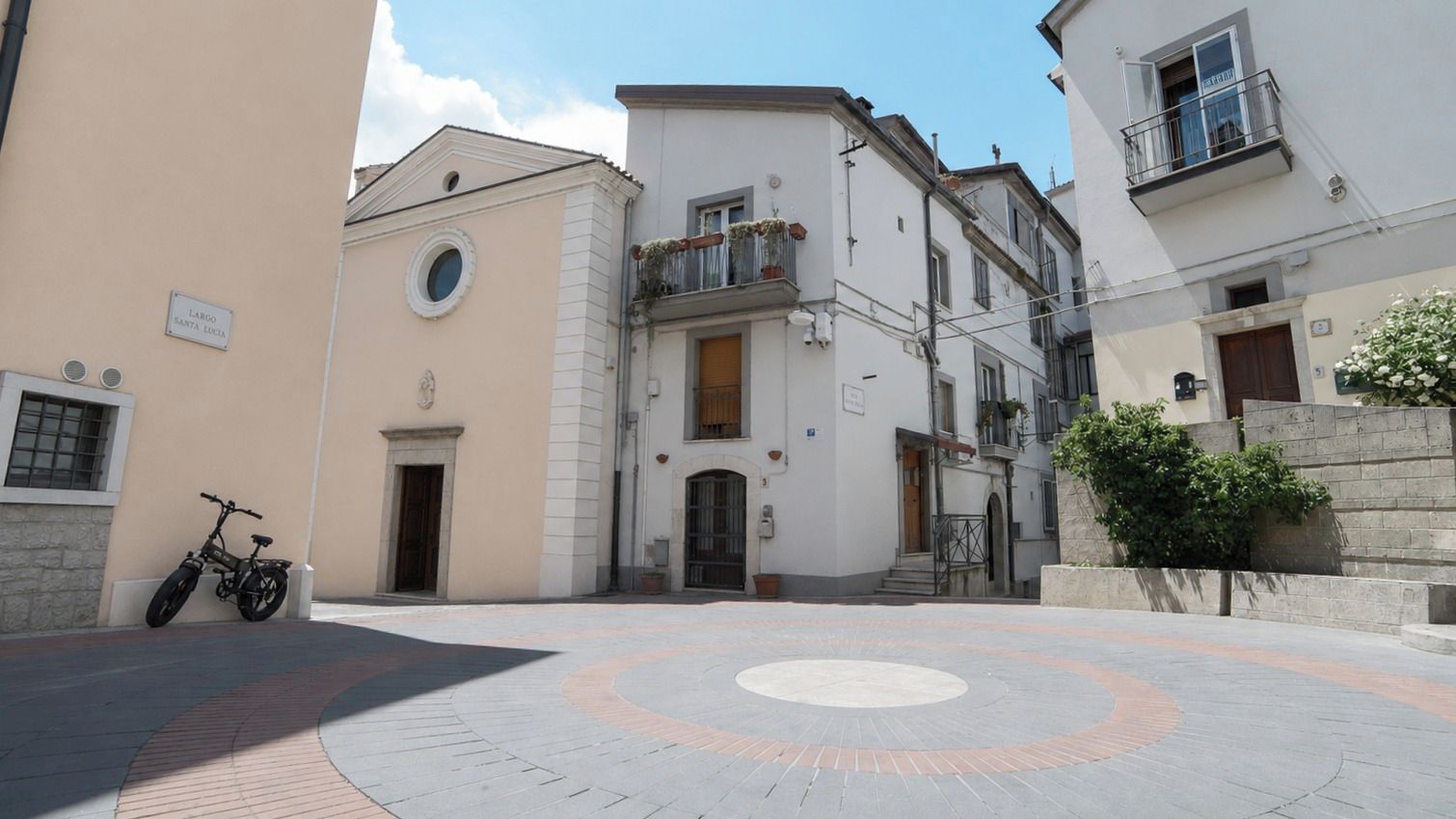 Un patio con una zona circular empedrada, un edificio con balcón y una bicicleta estacionada.