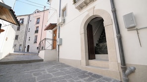 A narrow street with a stone staircase leading to a building with a white facade and an arched entrance.