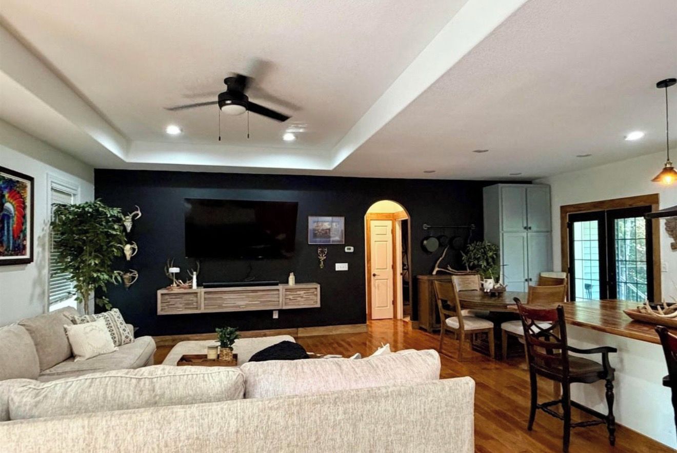 Ein modernes Wohnzimmer mit Flachbildfernseher, Deckenventilator und Essbereich mit Holzsesseln und Tisch.