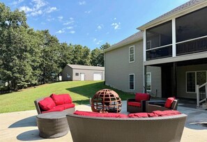 A residential property with a covered patio area featuring wicker furniture and red cushions, a large spherical decorative object, and a two-story house with a visible garage.