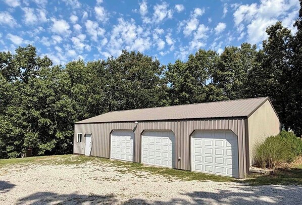 A single-story metal building with a flat roof, three garage doors, and a gravel driveway.