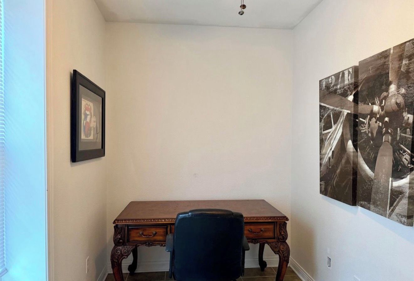 A room with a wooden desk, a chair, a framed picture on the wall, and a large black-and-white photograph.