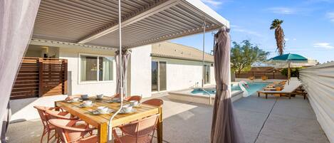 Un área de comedor al aire libre techada con piscina y sillas de descanso.