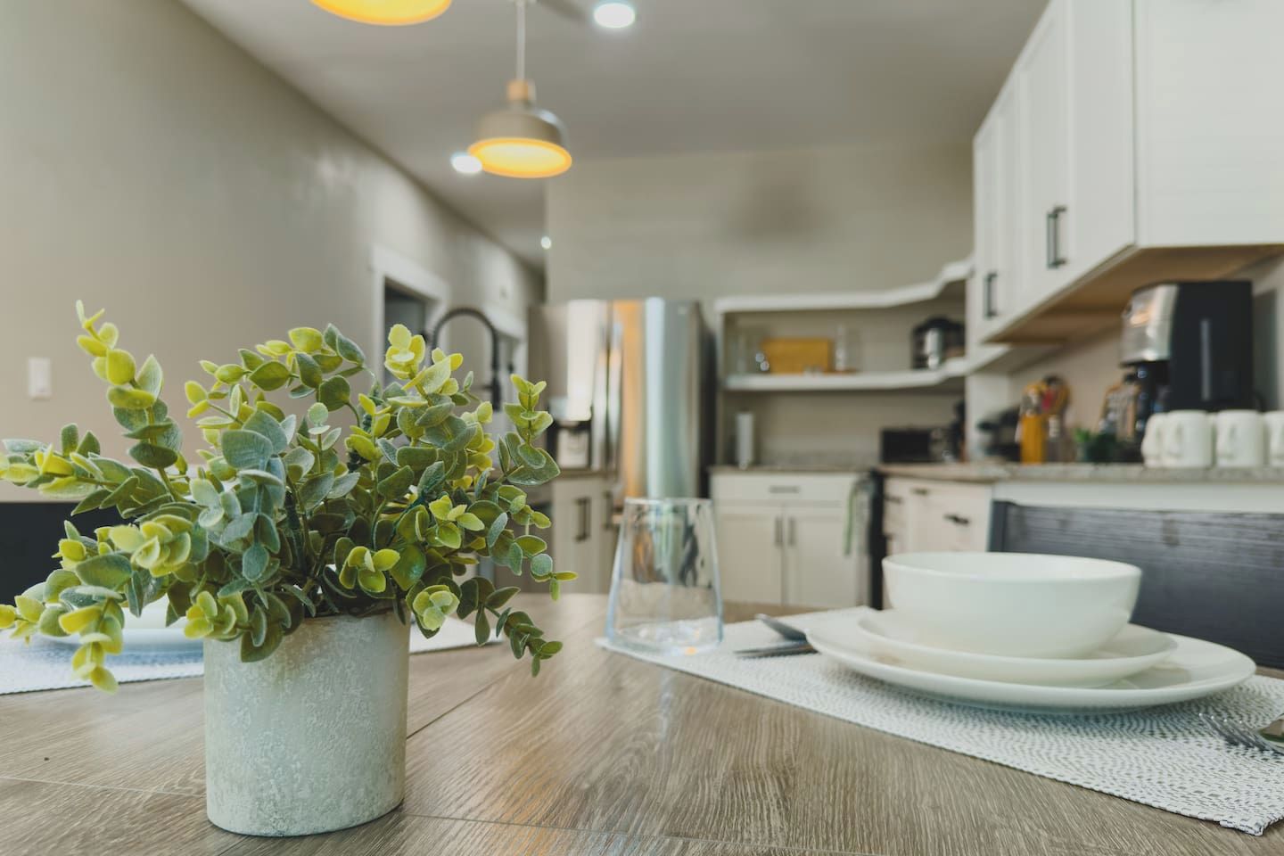 A dining area with a table, a potted plant, a glass, and plates.