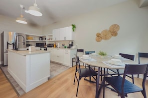 A modern kitchen with white cabinets, a central island, and a dining area with a round table and chairs. - Travelers Dream - 2 Homes 1 Stay (Colorado Springs)