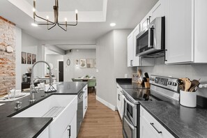Een moderne keuken met een centraal eiland, roestvrijstalen apparatuur en een accentmuur van baksteen.