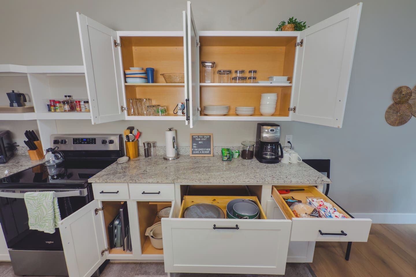 Una cocina compacta con armarios blancos, estufa integrada y cafetera.