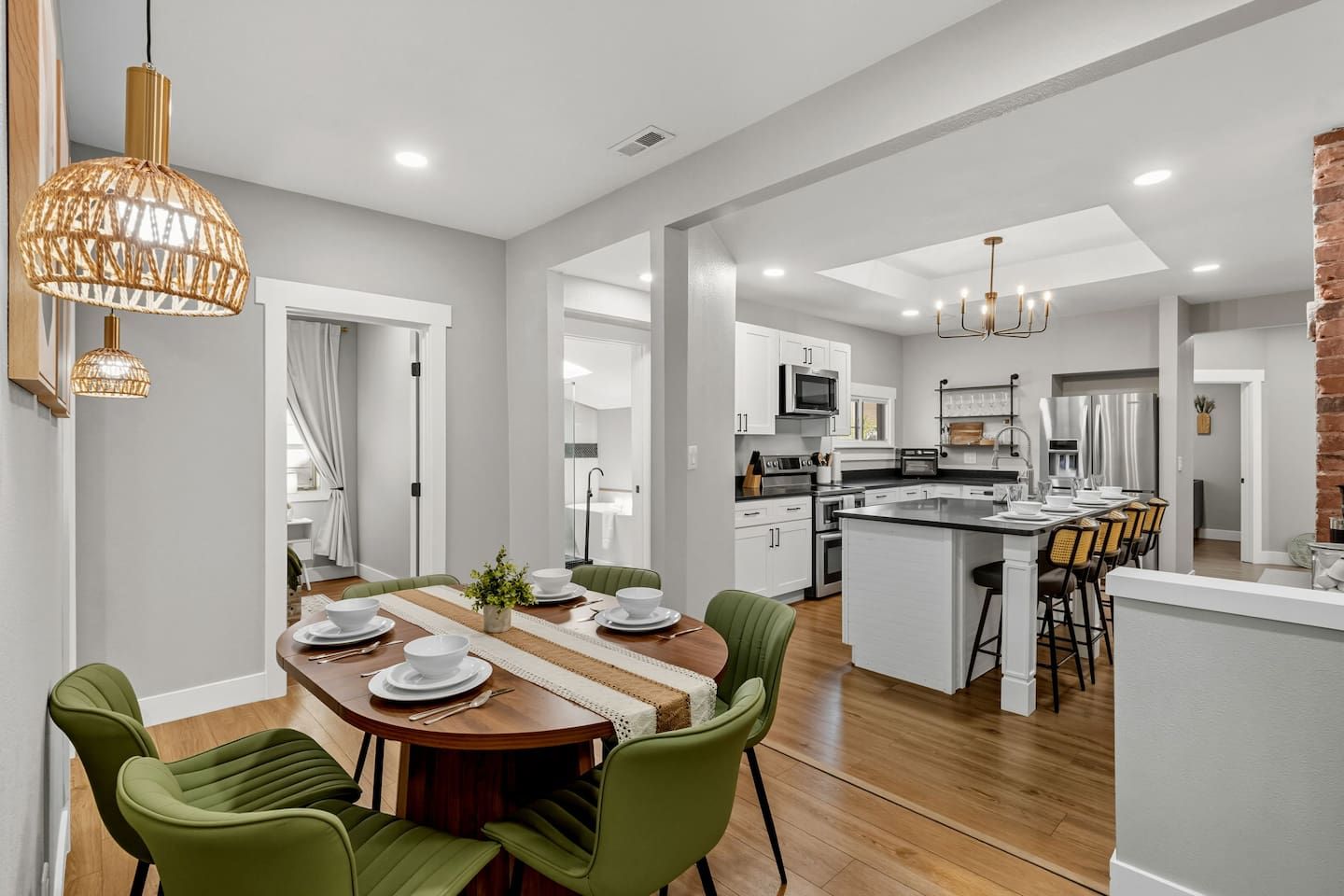 A modern kitchen with white cabinets, a central island, and a dining area with green chairs.