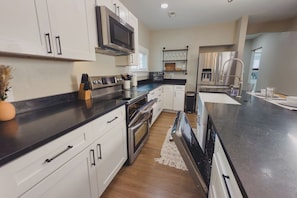 A modern kitchen with white cabinetry, stainless steel appliances, and a black countertop. - Travelers Dream - 2 Homes 1 Stay (Colorado Springs)