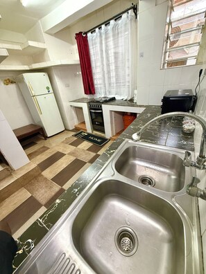 A compact kitchen with a refrigerator, stove, sink, and a window with curtains.