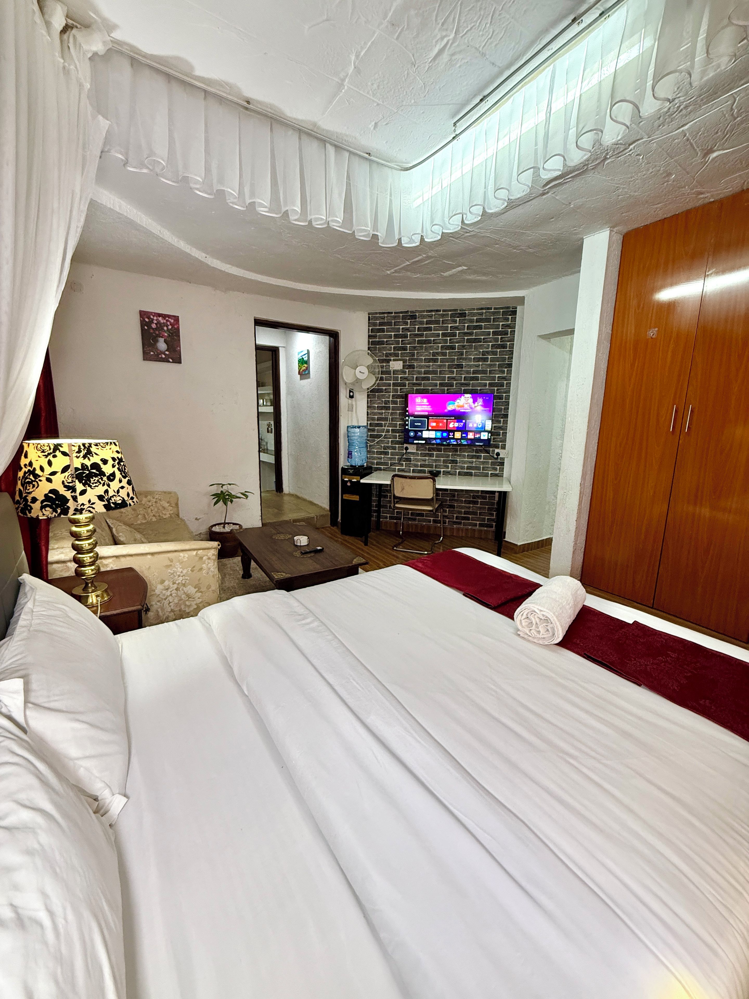 A hotel room with a bed, a desk, a chair, a television, and a wardrobe.