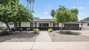 A modern two-story house with a paved driveway, a garage, and a landscaped front yard with various shrubs and a palm tree. - Private Pool & put put Oasis with a Great location (Scottsdale)