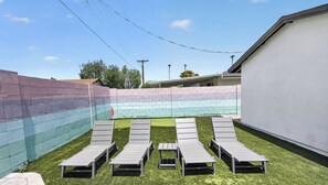 A backyard with a colorful brick wall, a white building, and six grey lounge chairs on artificial grass. - Private Pool & put put Oasis with a Great location (Scottsdale)