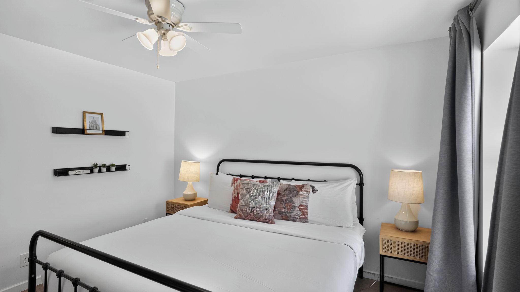 A bedroom with a bed, two bedside tables, a ceiling fan, and a wall-mounted shelf with decorative items.
