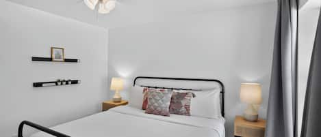 A bedroom with a bed, two bedside tables, a ceiling fan, and a wall-mounted shelf with decorative items.