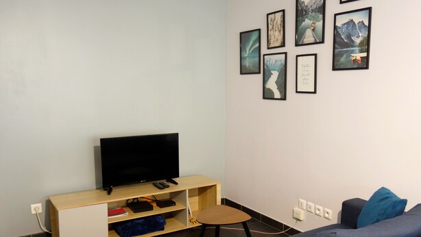 Uma sala de estar moderna com televisão de tela plana em um suporte de madeira, um sofá e uma parede decorada com quadros.