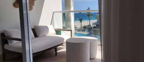 A modern room with a glass door leading to a balcony overlooking a beach.