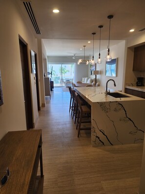 A modern kitchen with a marble island, pendant lighting, and a view to a balcony. - Oceanfront Luxury at Tortuga Bay · Infinity Pools hot tubs & 2 King Suites (San José del Cabo)
