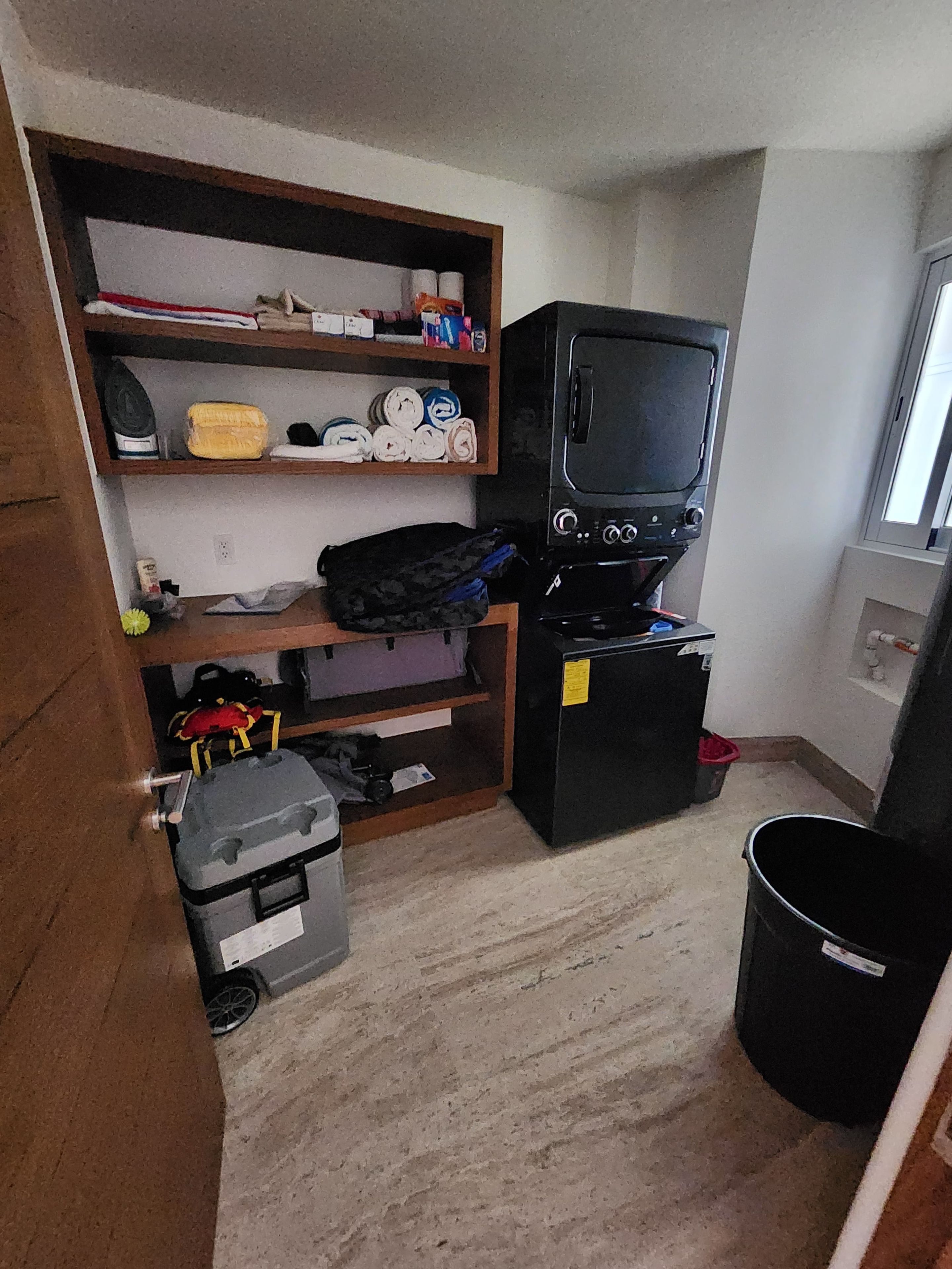 Habitación pequeña con televisión sobre un mueble, un escritorio y un cubo de basura.