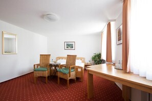 Quarto de hotel com cama, duas cadeiras, uma mesinha, espelho e um quadro na parede.
