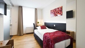 A hotel room with a bed, a desk, a chair, a TV, and a window with curtains. - Landgasthof Lamm (Aalen-Ebnat)